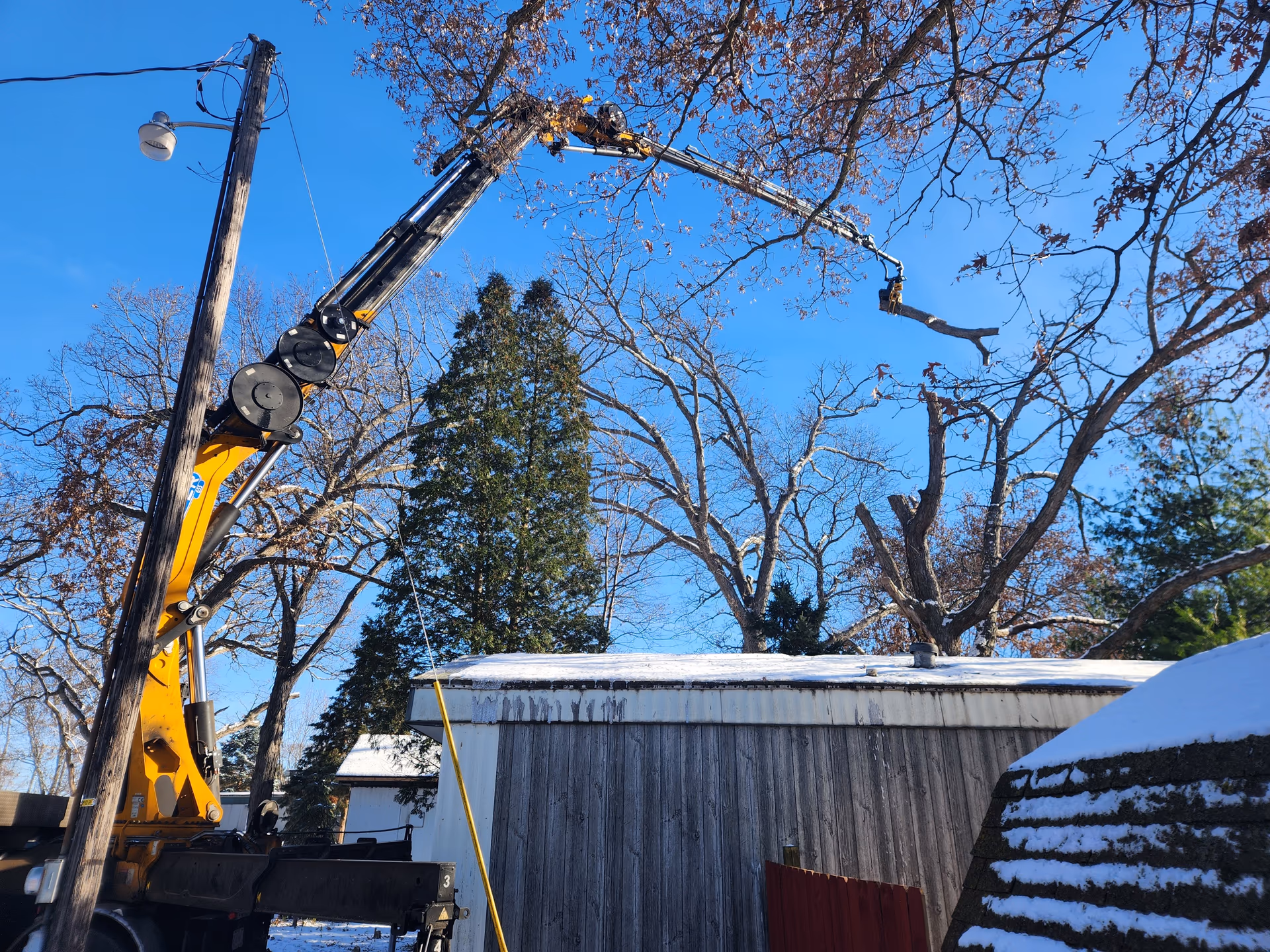 Crane lifting a fallen limb off a home during emergency tree service
