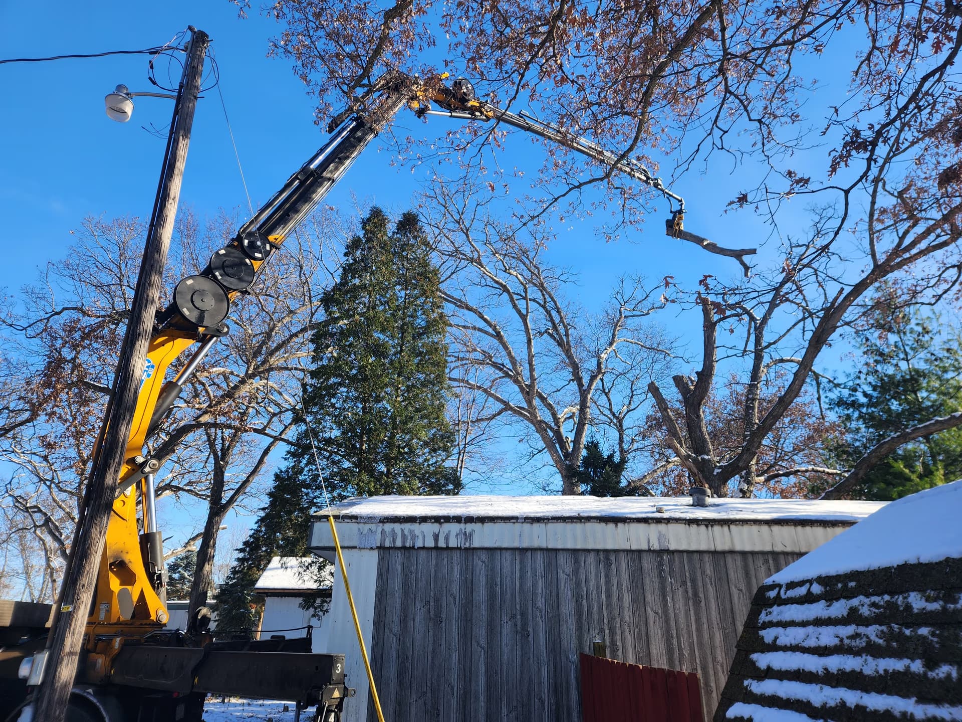 Crane lifting a fallen limb off a home during emergency tree service