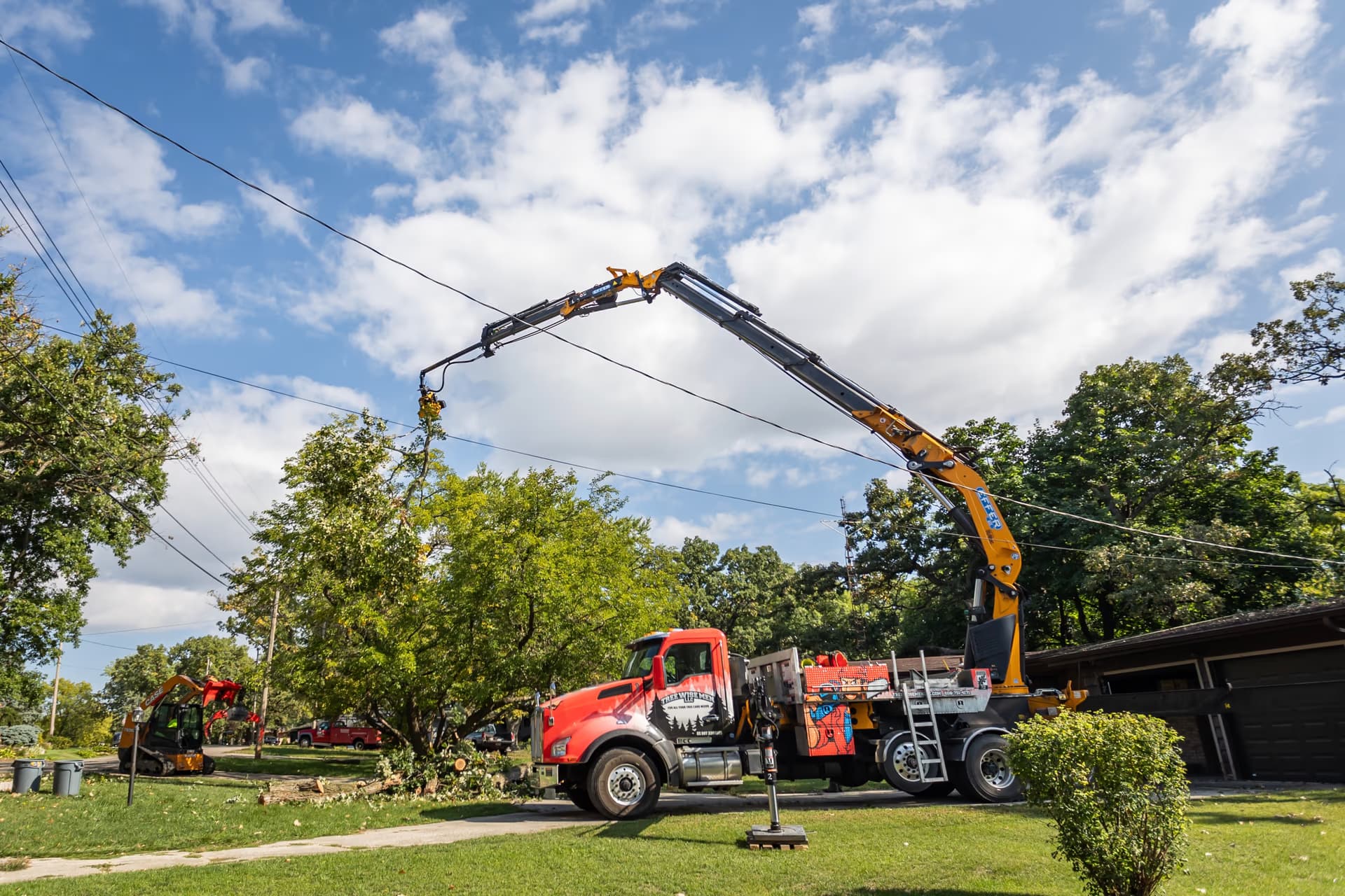 Crane truck with outriggers set on a residential lawn before pruning work