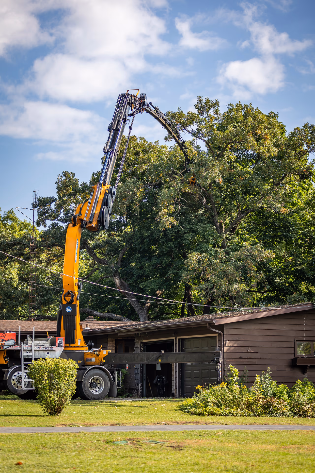 Grapple saw lifting a cut limb clear of a house roof