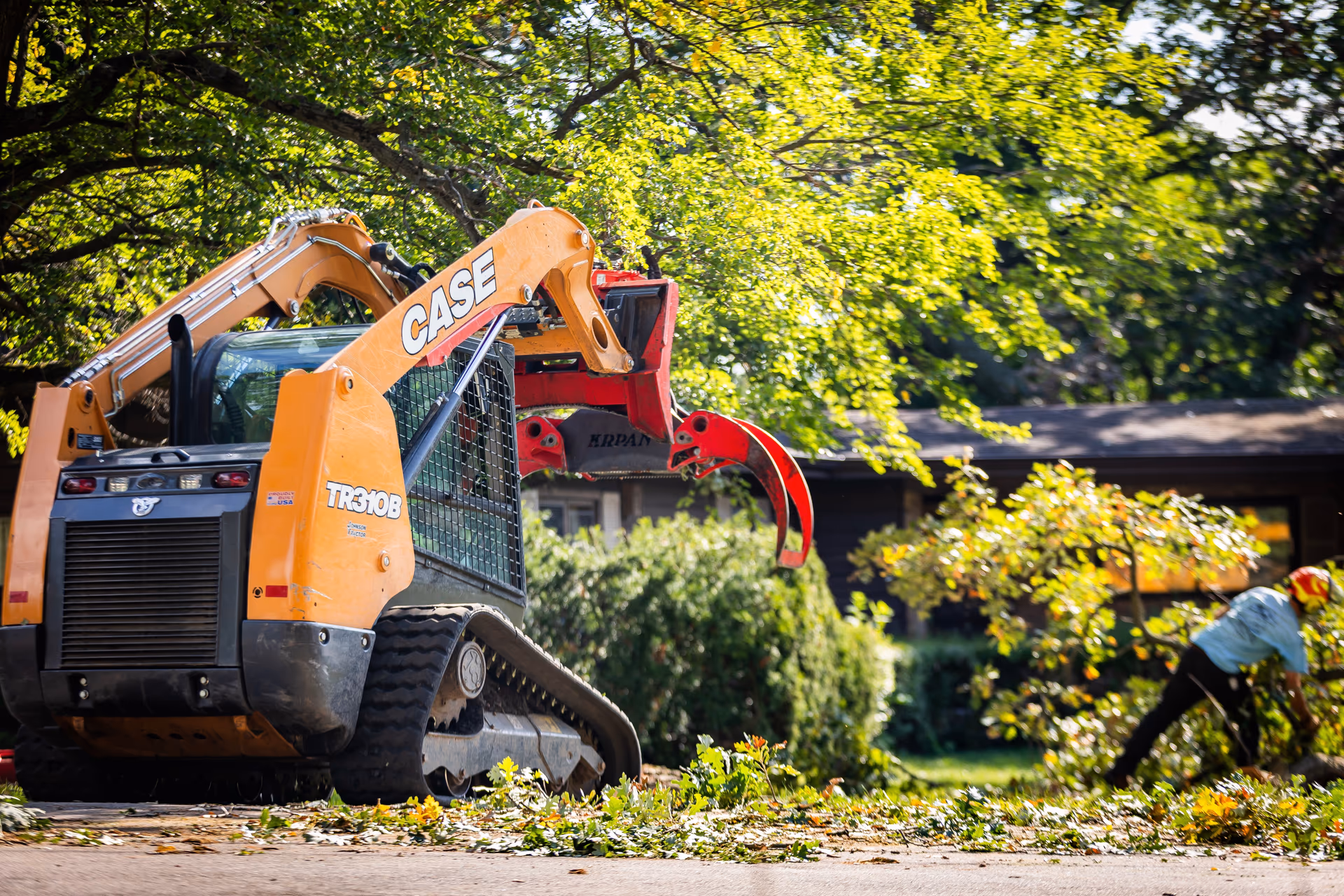 Skid steer grapple clearing brush and root debris from a yard