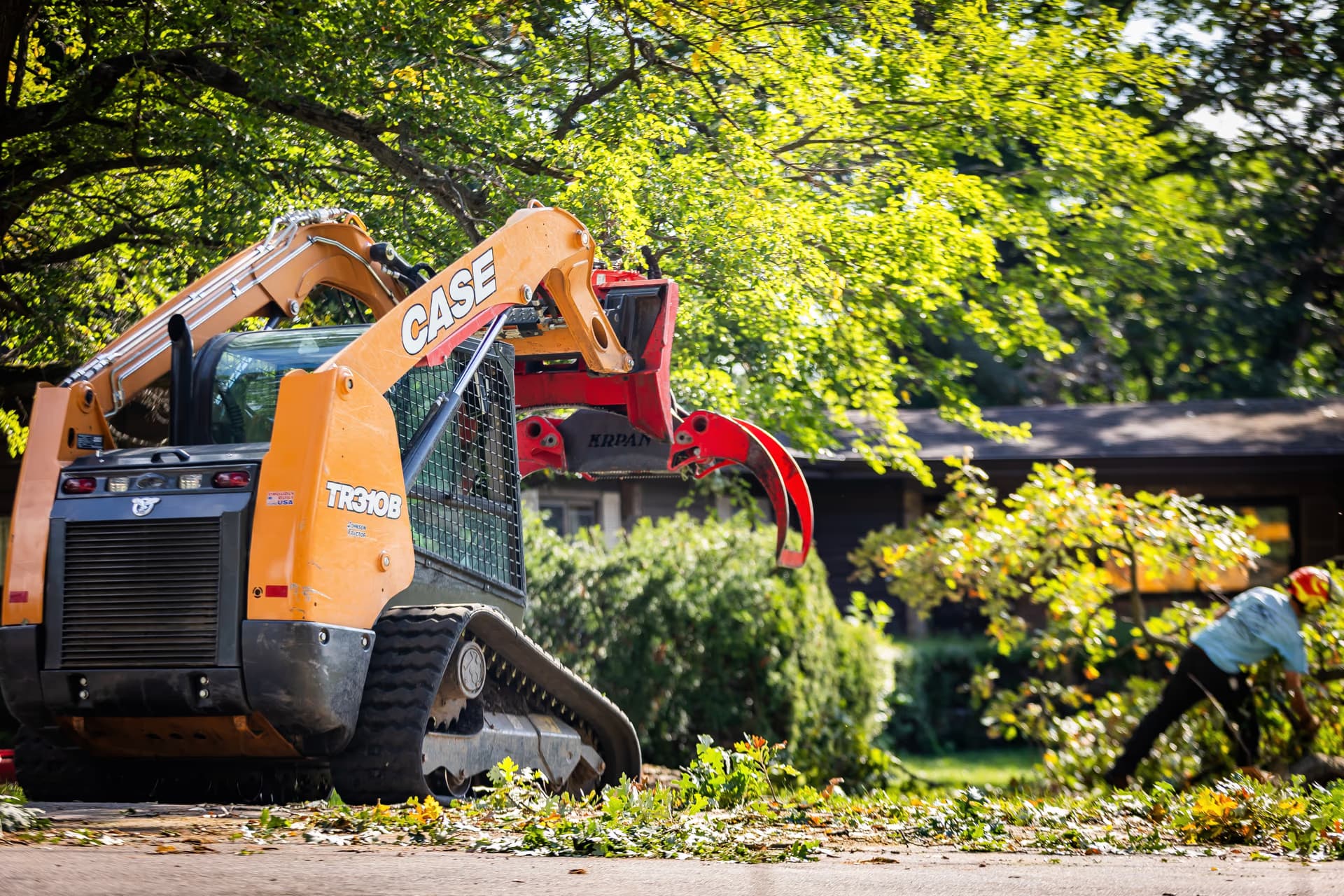 Skid steer with grapple clearing brush after a residential tree removal in Rock County
